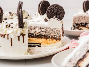 Oreo Ice Cream Cake on a Plate With Some of the Cake Cut Into Slices, and in the Surroundings, Slices on Two Plates and a Kitchen Towel on the Counter