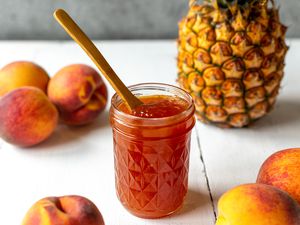 Peach and Pineapple Jam with a Spoon Surrounded by Peaches and a Pineapple