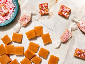Peppermint Caramels with Some Wrapped in Wax Paper, Some Topped with Crushed Candy Cane, and Some Without Toppings, All Next to a Small Bowl of Crushed Candy Canes