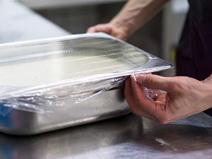 A cook stretching plastic wrap over a hotel pan in a restaurant kitchen