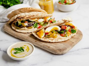Sabich Sandwiches on a Wooden Plank Next to a Bowl of Tahini