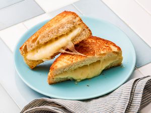 Sheet Pan Grilled Cheese Sandwich Cut in Half and on a Light Blue Plate Next to a Table Napkin