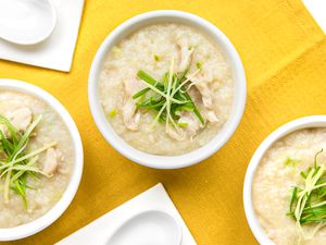 Bowls of Chicken Congee Topped with Sliced Ginger and Green Onions, Next to Soup Spoons, All on a Mustard Colored Kitchen Towel