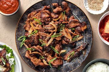 Spicy pork bulgogi on a platter, surrounded by condiment bowls