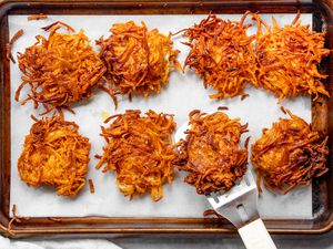 Sweet Potato Latkes on a Parchment Lined Baking Sheet with One on a Spatula
