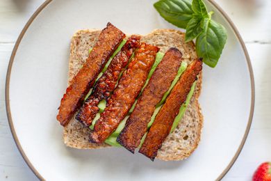 Overhead view of vegetarian bacon on a piece of bread with avocado underneath it.