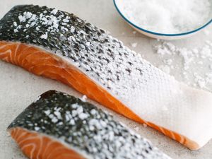 Two Salmon Fillets With Skin Salted Using Coarse Salt, and Next to It, More Salt in a Bowl and Some on the Counter 