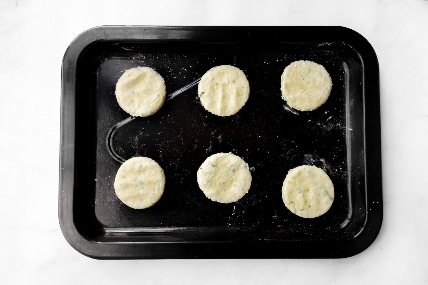 Six biscuits on a black sheet pan. 