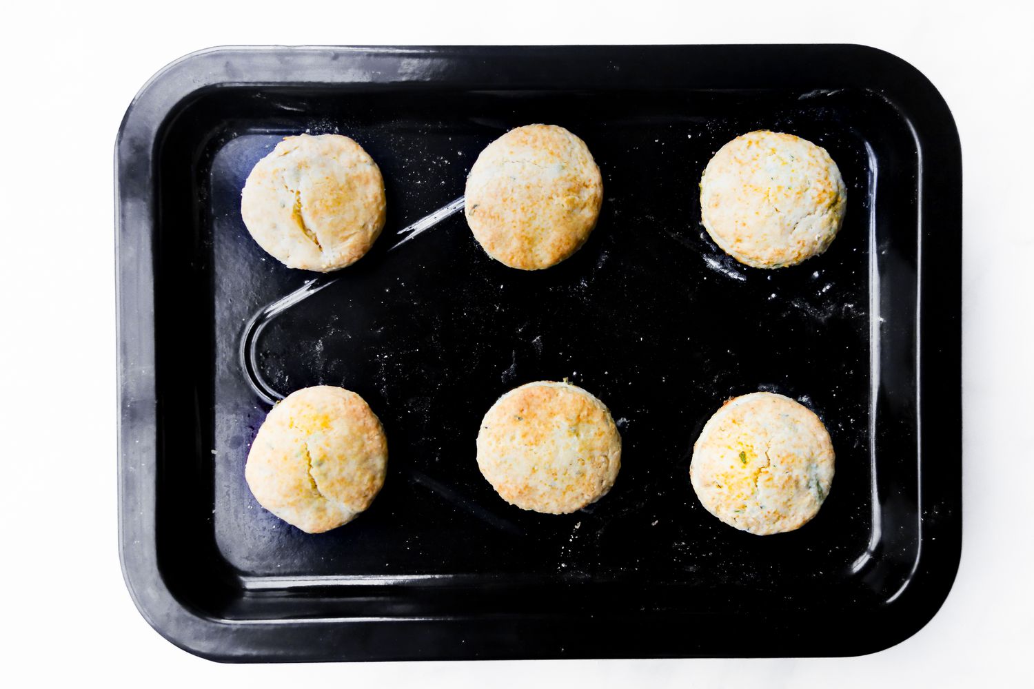Six baked biscuits on a black sheet pan.