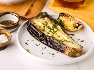 Plate of Whole Grilled Eggplant Next to a Platter of More Eggplant and an Oil Dispenser