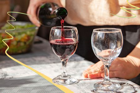 Pouring red wine into a glass on a tableclothed table outside