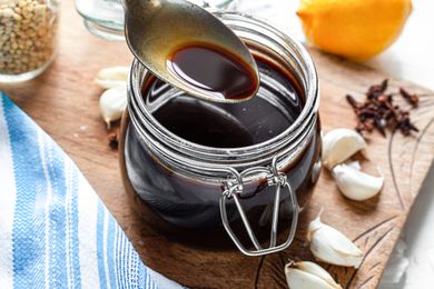 Spoonful of Worcestershire Sauce Lifted from a Jar Sitting on a Decorative Wooden Board Covered in Garlic Cloves and Cloves