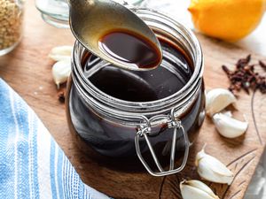 Spoonful of Worcestershire Sauce Lifted from a Jar Sitting on a Decorative Wooden Board Covered in Garlic Cloves and Cloves