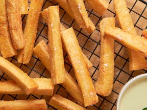 Yuca Fries on a Cooling Rack With a Bowl of Spicy Mayo, and Underneath the Cooling Rack, Parchment Paper