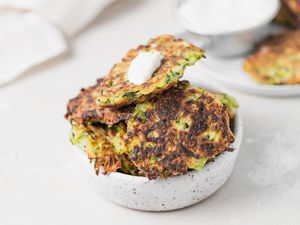 A bowl of zucchini fritters set on a white background.