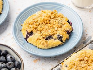 Blueberry Muffin Top on a Plate, Surrounded by a Bowl of Blueberries, More Muffin Tops on a Wire Rack, a Glass of Milk, and Another Muffin Top on a Plate