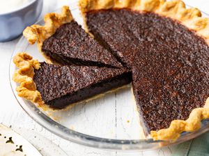 Chocolate Chess Pie With Some Cut Into Slices in a Pie Dish, and in the Surroundings, a Pie Server and a Bowl With Whipped Cream