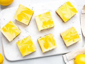 Lemon Cheesecake Bars on a Marble Board, and on the Counter, Lemons and a Kitchen Towel